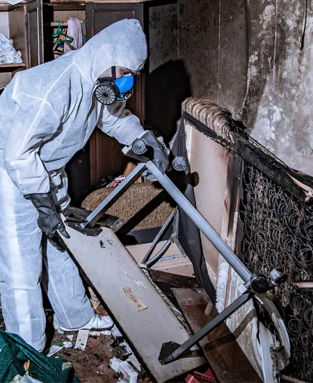 A technician in protective gear clearing smoke damaged contents from a burned room