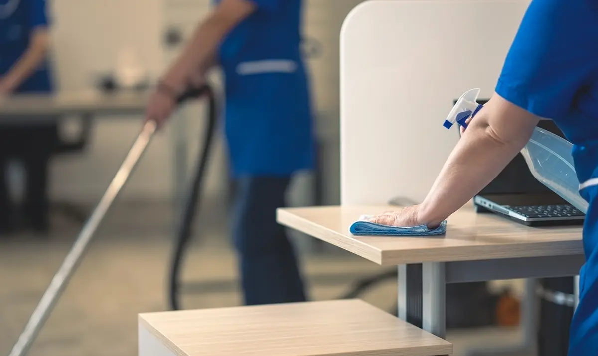 A cleaning crew wiping down desks in an open plan office